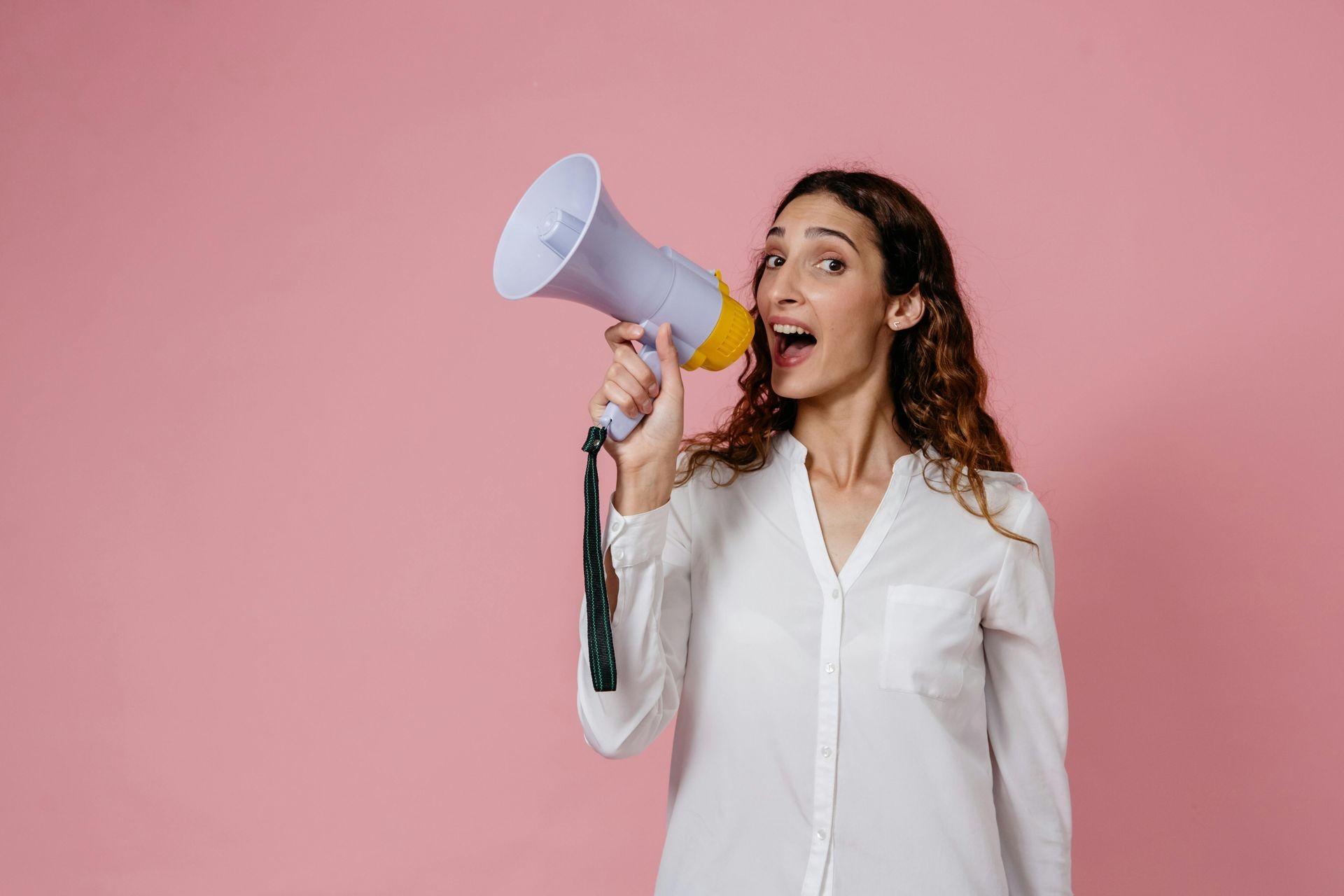 Woman holding a megaphone against a pink background, wearing a white shirt.